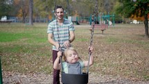 father pushing his daughter on a swing set 