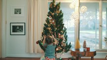toddler girl hanging an ornament on a Christmas tree 