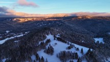 A snowy mountain covered in trees, seen from above, with the sky, clouds, aerial Hyperlapse