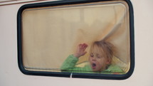 A 5-year-old girl blows on the window of the van and draws with her fingers on the foggy glass
