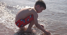 Young boy washing shells on beach in summer