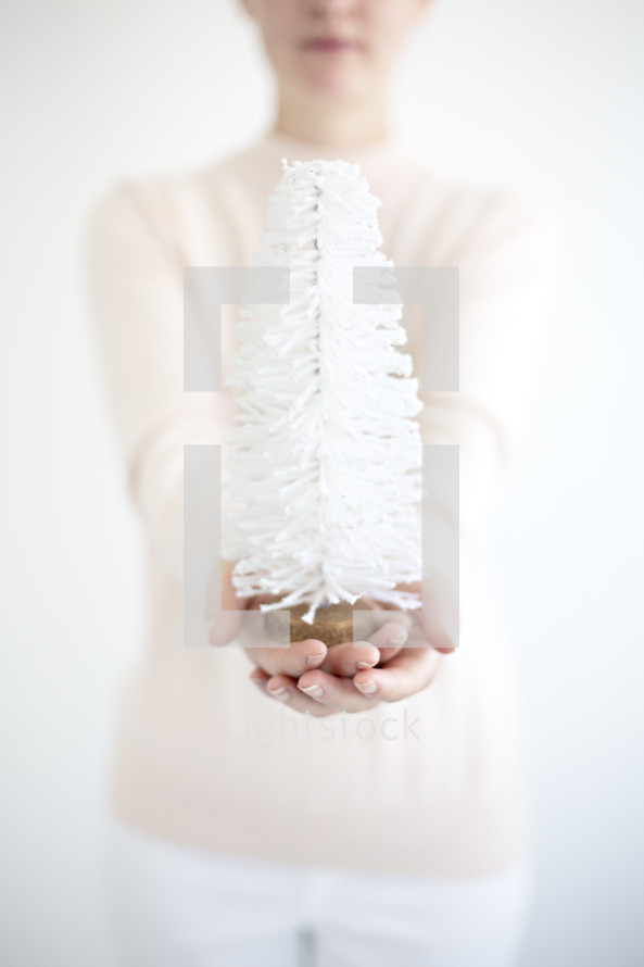 a woman holding a white bottle brush Christmas tree