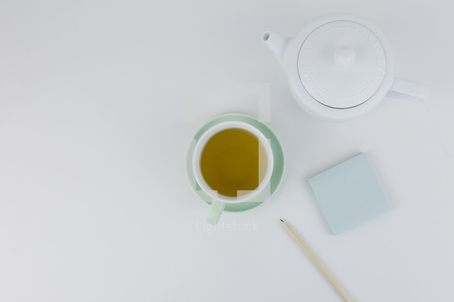 notepad, tea pot, cup, saucer, and pencil on a white background 