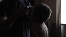 A young child, small, cute boy being dressed by his father in cinematic slow motion as his father puts on his shirt.