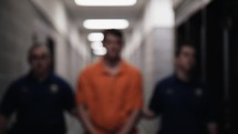 Prisoner shackled in handcuffs and wearing orange prison uniform is led in cinematic slow motion to his prison cell by prison guards.