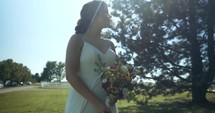 Bride in white dressing with flowers in sunlight on wedding day.