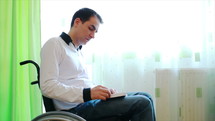 Young man in wheelchair reading the Bible at home near the window