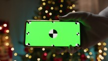 Santa Claus holding a smartphone in front of the tree, green screen