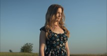 Young woman in flower dress watching sunset in summer nature.