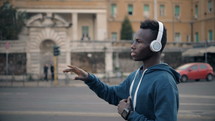 young man listening to headphones walking down a street 