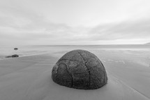 A large round boulder on a sandy beach.