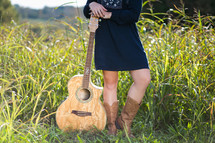 young woman standing in a field with a guitar 