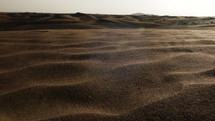 Wind blowing sand and dust over middle eastern desert sand dunes in United Arab Emirates landscape in cinematic slow motion.