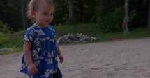 Young toddler girl walks on  small lake side beach exploring