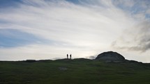 A Couple Walking By Dartmoor Tor As Sun Sets In Background