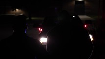 Silhouette of a man being arrested in front of flashing police officer, cop car lights at night in slow motion.