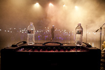 Man performing on stage behind two water bottles on an amp.