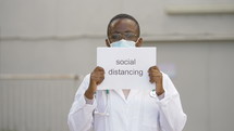 a healthcare worker holding up a sign that reads social distancing 