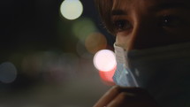 a woman in a city at night wearing a face mask 