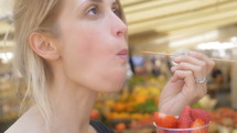 Blonde woman eating strawberries at a farmer's market.