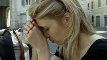 Blonde woman resting her forehead on her hands.