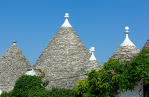 Traditional conical rooftops of trulli houses are made of piled stone slabs and decorated with white pinnacles against a blue sky