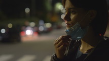 a woman in a city at night wearing a face mask 