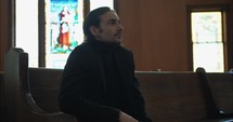 Sombre, sad, melancholy man sitting alone in church in prayerful contemplation.