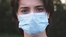 Brunette woman staring into camera wearing a medical mask.