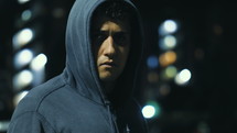Man wearing a hoodie at nighttime staring ominously into camera.