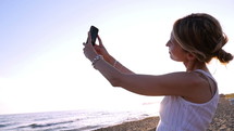 Woman taking a selfie on the shore of a beach.
