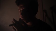Troubled young man, teenage boy smoking drugs or cigarette, getting high, in dark, smoky room in cinematic slow motion lighting joint.