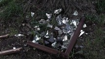 Broken, shattered shards of glass from mirror laying in grass on ground in cinematic slow motion. 