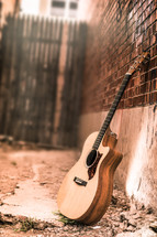 An acoustic guitar in an alley. Guitar. Acoustic guitar. Guitar on wall. Music. Praise and Worship. Acoustic. Guitar Lessons. Tryouts. 