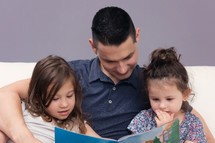 Man Reading a book to his two daughter 