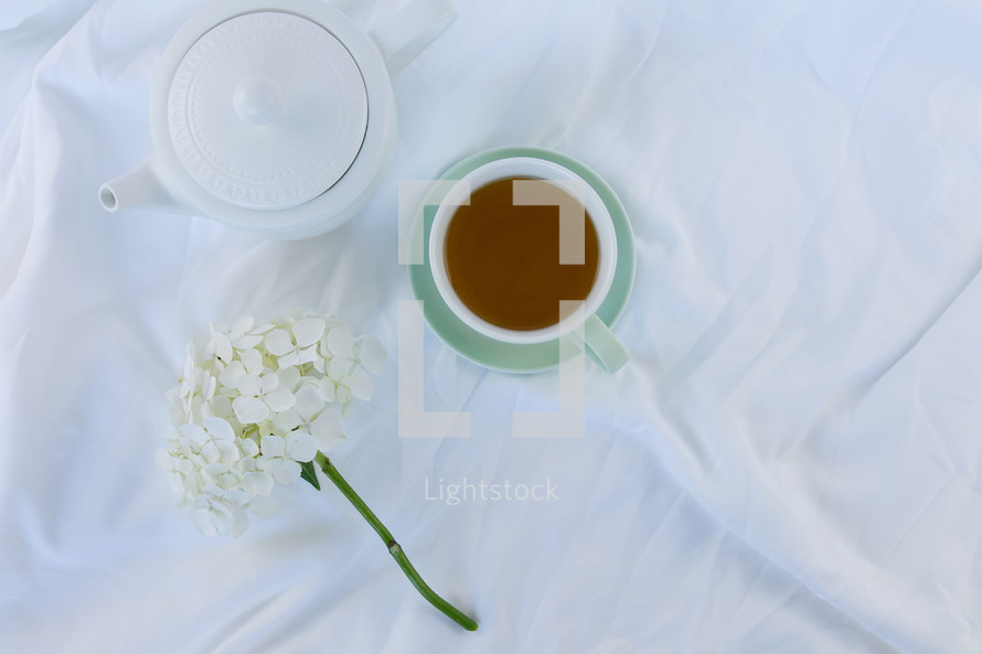 tea pot, cup of tea, and flowers on sheets on a bed 