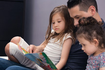 Man Reading a book to his two daughters 