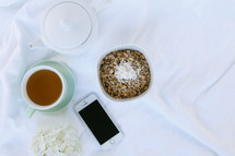 tea pot, cup of tea, oatmeal, flowers and cellphone on bed sheets