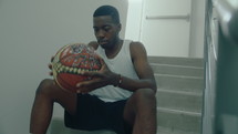 Athlete Sitting on Stairs and Handling Basketball

