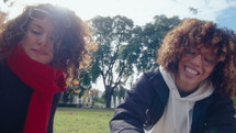 Two happy female friends smiling and petting adorable dog lying on his back on blanket, spending time on green lawn in the park
