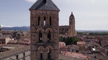 Aerial View Of Church Tower Of San Esteban With View Of Segovia Cathedral In Background On Sunny Day. Ascending Shot