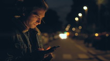 man frantically texting standing in a city at night 