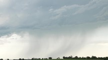 Rainfall in stormy, cloudy sky on farmland in the summer. Raining from storm clouds on grassland in farming community during thunderstorm in cinematic slow motion.