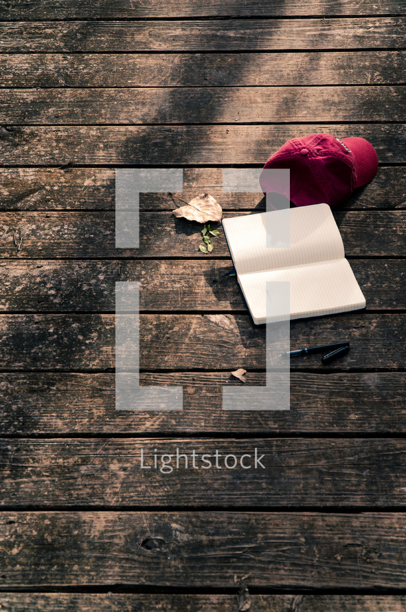 a ball cap, open journal, and pen on a wood deck 