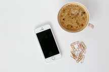 latte in a mug, cellphone and gold paperclips 