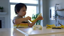 Toddler boy peeling bananas on kitchen counter  - wide shot
