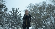 Woman in winter coat standing outside in Christmas, winter snow as snowflakes fall in cinematic slow motion.