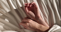 Womans hands lay across bed in summer sun - blissful - sleeping in