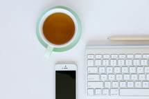 tea cup, computer keyboard, pencil, and cellphone on a desk 