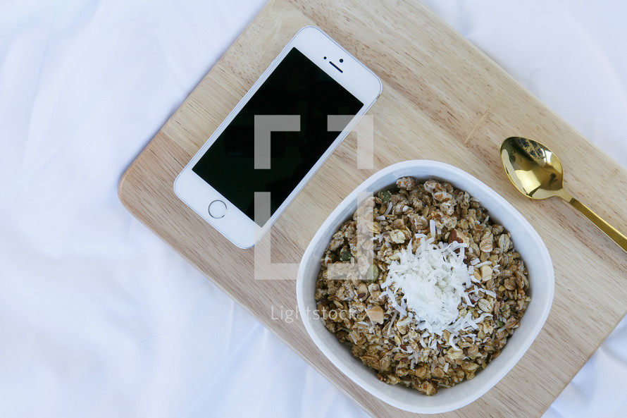 iPhone, bowl of oatmeal, and spoon on a wooden tray 